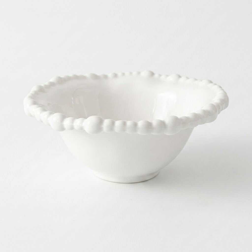 An empty white bowl with a raised beaded rim and small circular foot rests against a pale background.