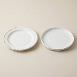 Two small white ceramic plates on a warm beige background, one with a beaded rim and one plain.