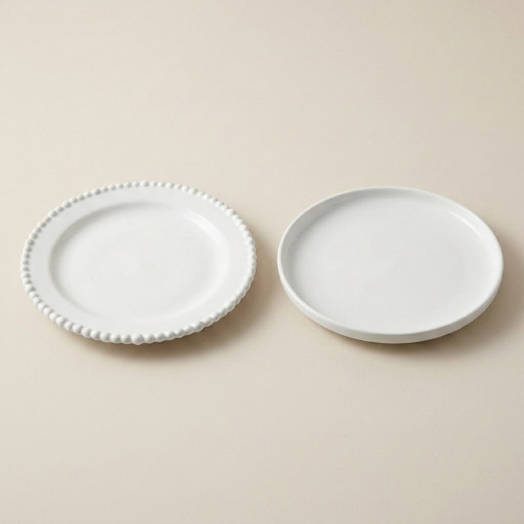 Two small white ceramic plates on a warm beige background, one with a beaded rim and one plain.