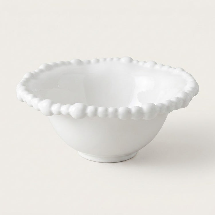 A white ceramic bowl with a scalloped, beaded rim, photographed on a clean, solid off-white background.