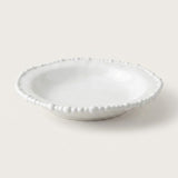 A small white ceramic dish with a scalloped beaded rim, photographed on a clean, solid, warm off-white background.