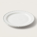 A white ceramic plate with a decorative beaded border, photographed on a clean, light beige background.