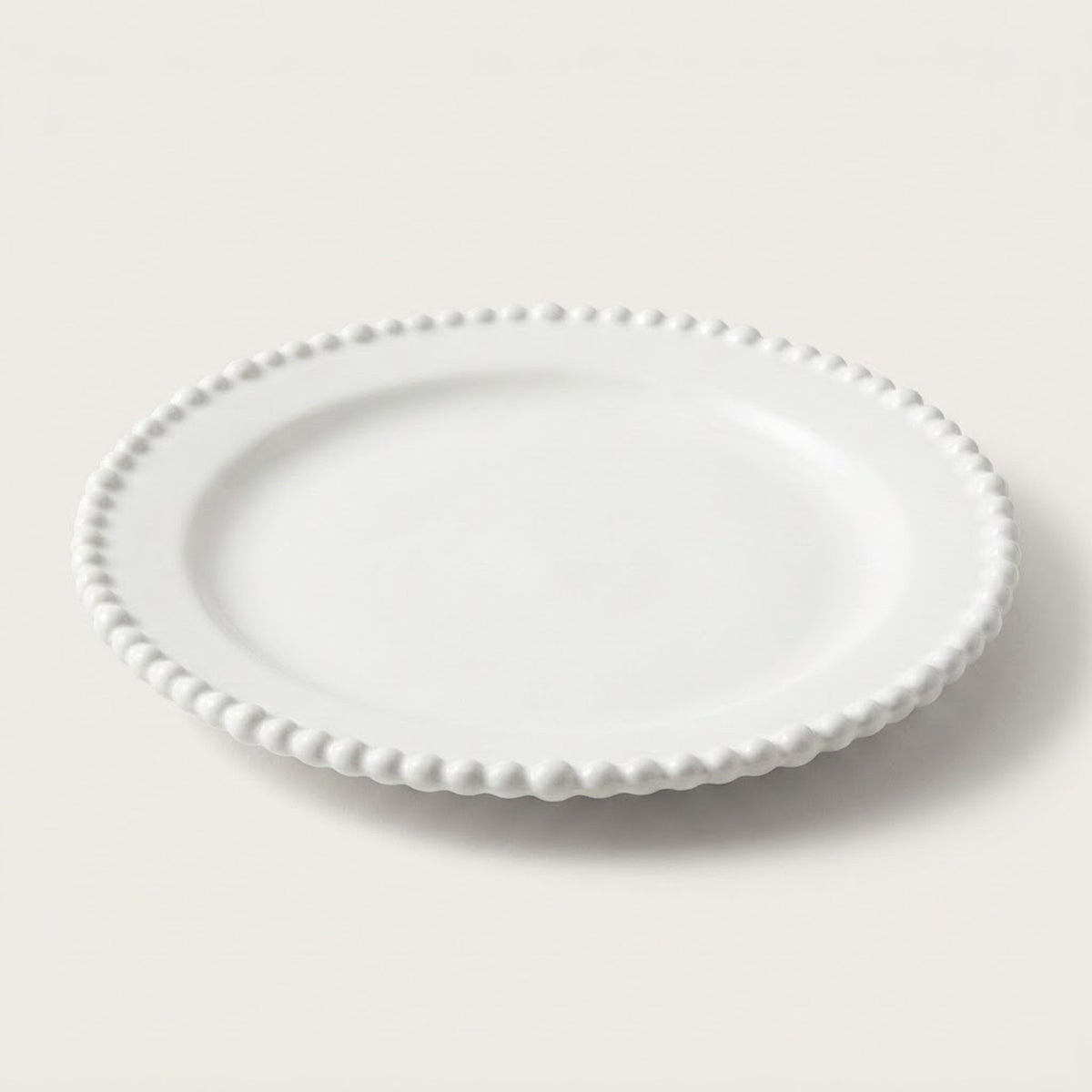 A white ceramic plate with a decorative beaded border, photographed on a clean, light beige background.