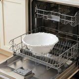 A white bowl with a raised beaded rim sits in the extended lower rack of an open dishwasher.