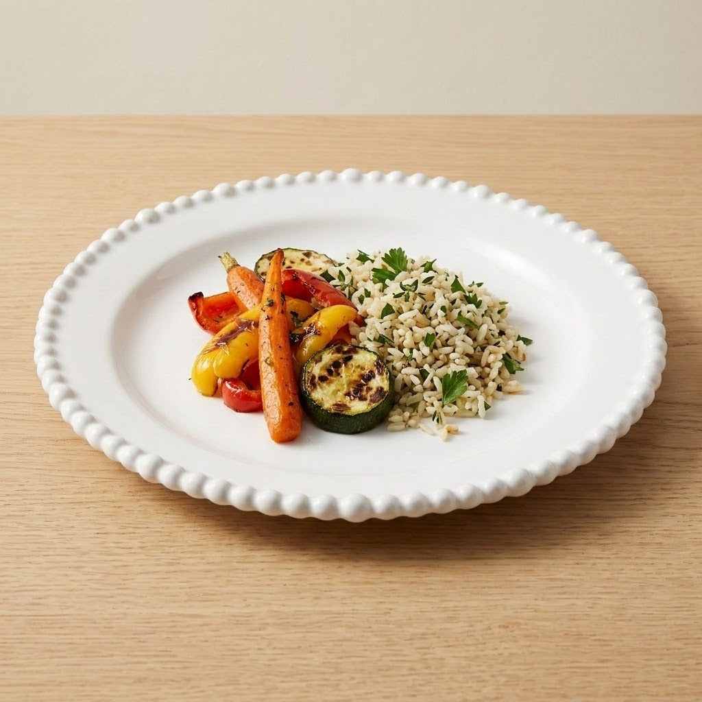 A white beaded-rim plate holds rice with herbs and roasted vegetables on a light wooden table.