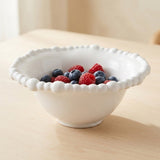 A white bowl with a raised beaded rim holds blueberries and raspberries on a sunlit wooden table.
