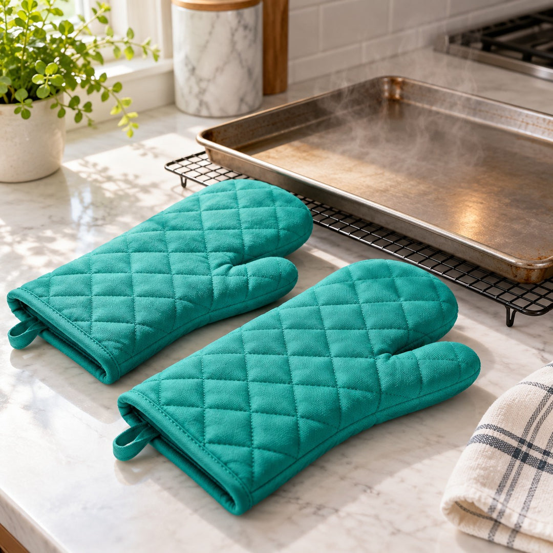 Turquoise cotton blend oven mitt pair beside a hot baking tray on a kitchen counter.