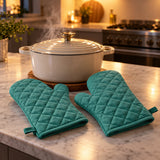 Turquoise oven mitt pair beside a steaming covered casserole pot on a kitchen island.