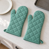 Turquoise oven mitt pair laid beside a dinner plate and baking tray to show their scale.
