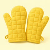 Pair of yellow quilted cotton blend oven mitts centered on a pale yellow studio background.