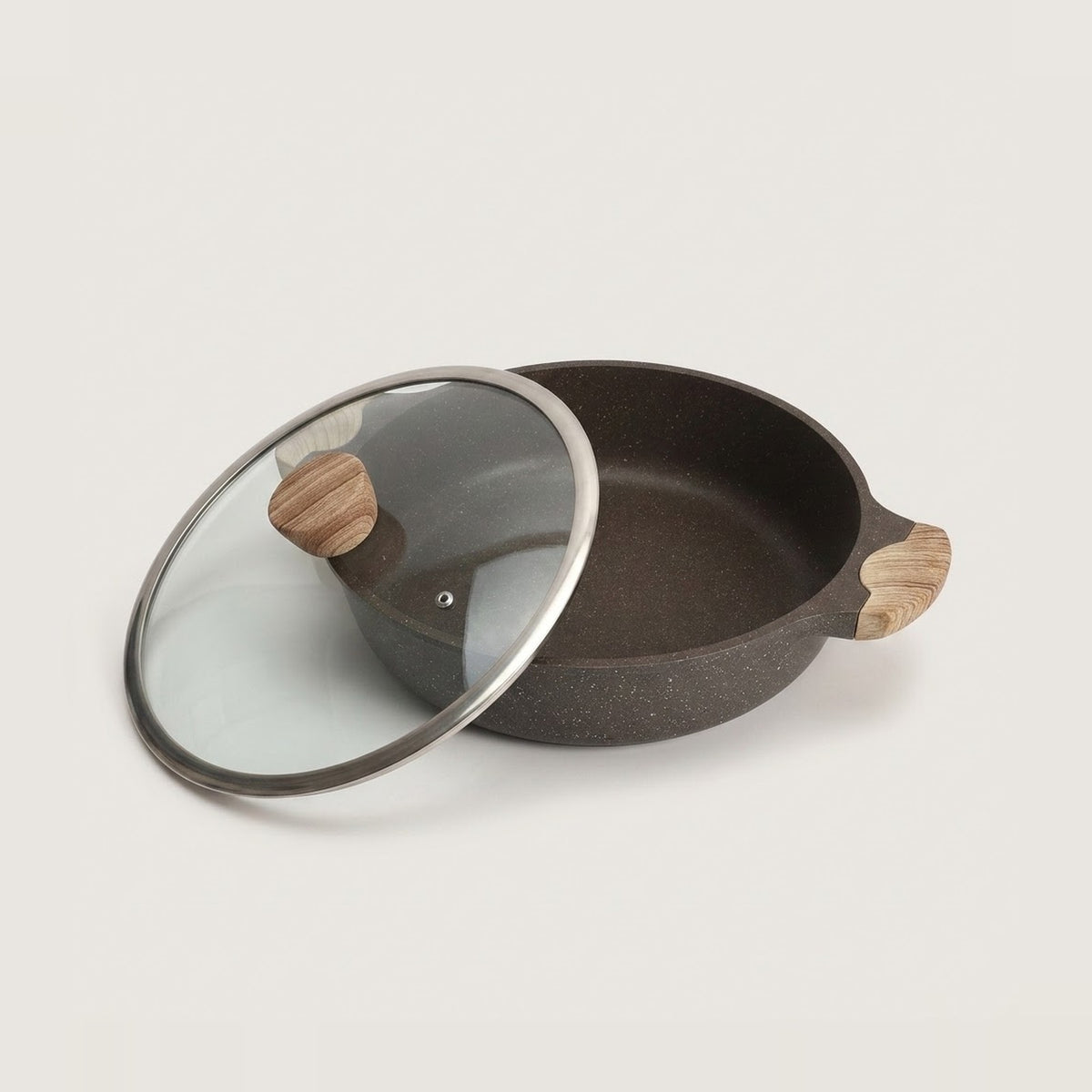 A dark speckled non-stick pan with a matching glass lid featuring a silver rim and light wood handles, shown on a clean off-white background.