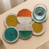 Six overlapping round coasters display colorful geometric patterns on a wooden tabletop, with a water glass resting on the teal sunburst design.