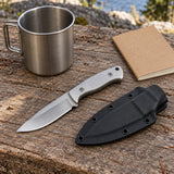 Silver steel fixed blade knife and sheath sit beside a camp mug and blank field notebook for scale.