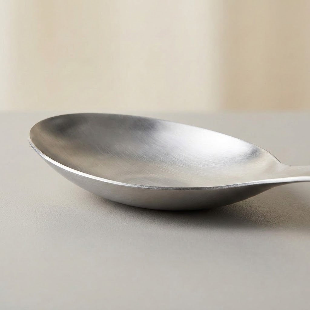 A brushed silver metal spoon resting on a neutral gray surface with a soft beige background.