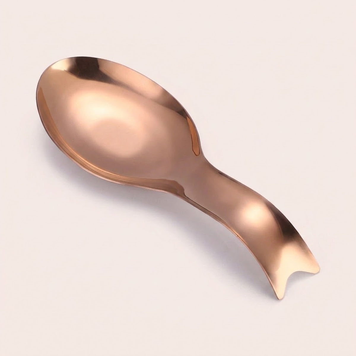 A modern, sculptural spoon-shaped object with a reflective rose gold metallic finish, photographed on a clean, solid off-white background.