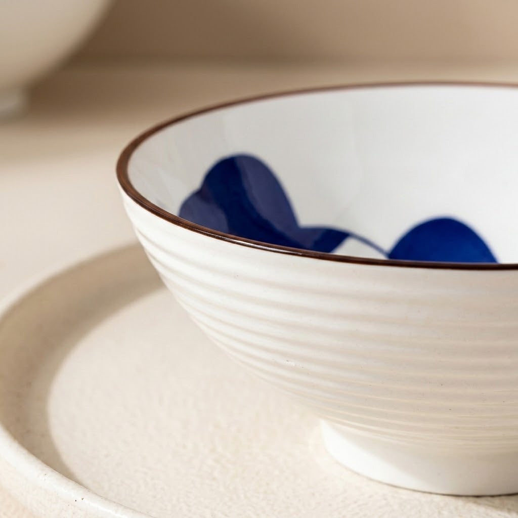 Close-up of a white ceramic bowl showing its ridged exterior, brown rim, and blue interior decoration on a cream tray.