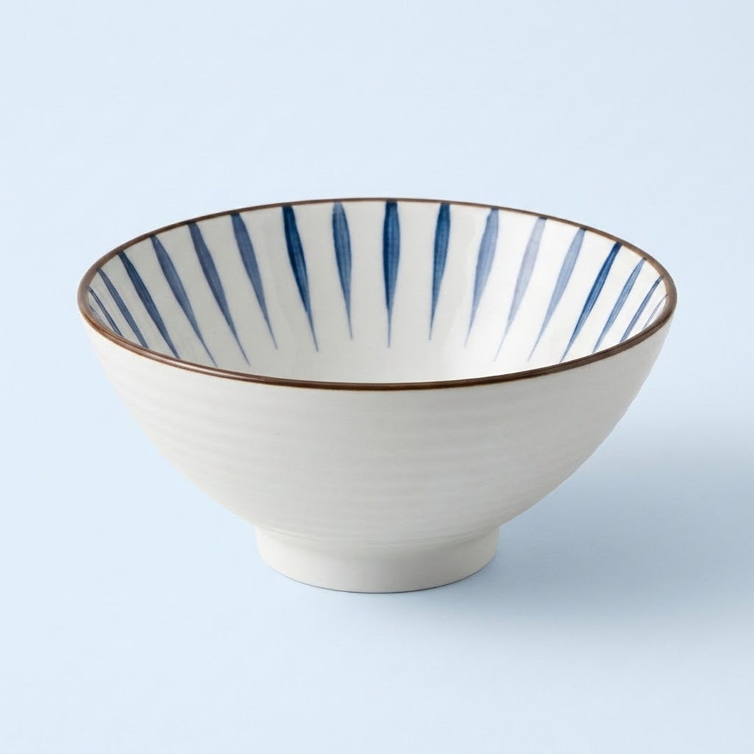 White ceramic bowl with tapered blue interior stripes and a thin brown rim sits against a pale blue background.