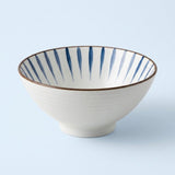 White ceramic bowl with tapered blue interior stripes and a thin brown rim sits against a pale blue background.