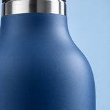 Close detail of the blue bottle's smooth matte coating and reflective stainless steel neck.