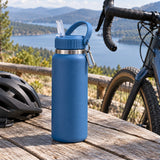 Blue insulated straw bottle stands beside a bicycle at a quiet outdoor cycling rest stop.