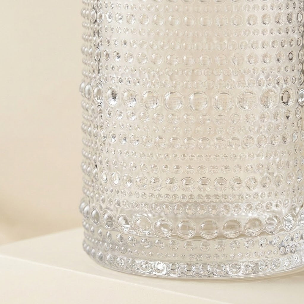 A close-up of a clear glass container with a textured, bubbly bubble pattern on a warm cream background.