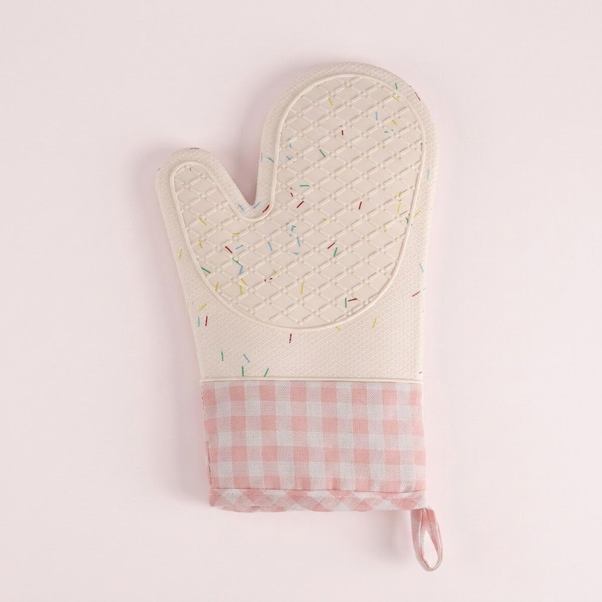 A quilted oven mitt in cream with a multicolor sprinkle pattern on the top half and a pink and white gingham check pattern on the bottom cuff, featuring a small pink loop at the wrist, shown on a light pink background.