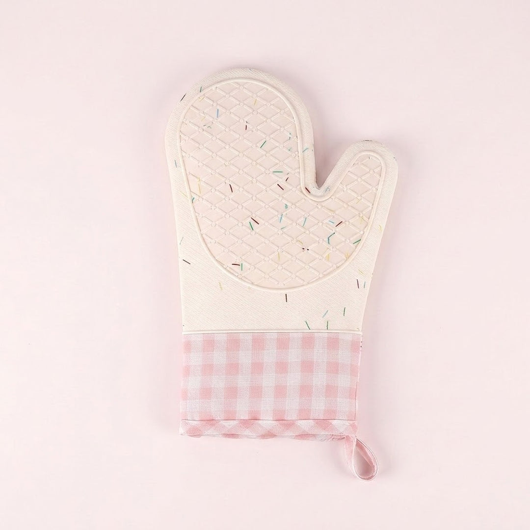 A quilted oven mitt with a cream-colored top section featuring a subtle multicolor sprinkle pattern, and a pink and white gingham checkered bottom section with a matching fabric loop, set against a solid pale pink background.