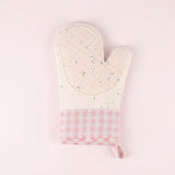 A quilted oven mitt with a cream-colored top section featuring a subtle multicolor sprinkle pattern, and a pink and white gingham checkered bottom section with a matching fabric loop, set against a solid pale pink background.