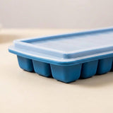 A close-up of a blue silicone ice cube tray with a matching translucent lid, resting on a light beige surface.