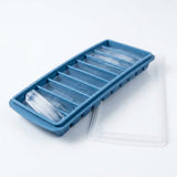 A blue tray holds long ice sticks, with one resting diagonally across a compartment and a translucent lid beside it.