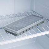 A gray ice stick tray covered with a translucent lid rests on a white wire shelf inside a freezer.