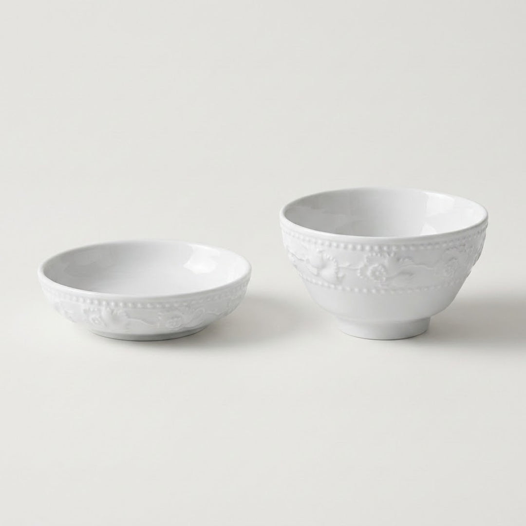 Two white ceramic bowls with embossed floral patterns, one shallow and one deeper, on a light gray background.