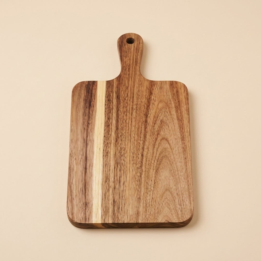 A rectangular wooden cutting board with rounded corners and a handle, featuring natural wood grain patterns in shades of brown and beige, set against a solid light beige background.