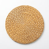 A round woven straw placemat in a natural light tan color, photographed from directly above on a clean white background.