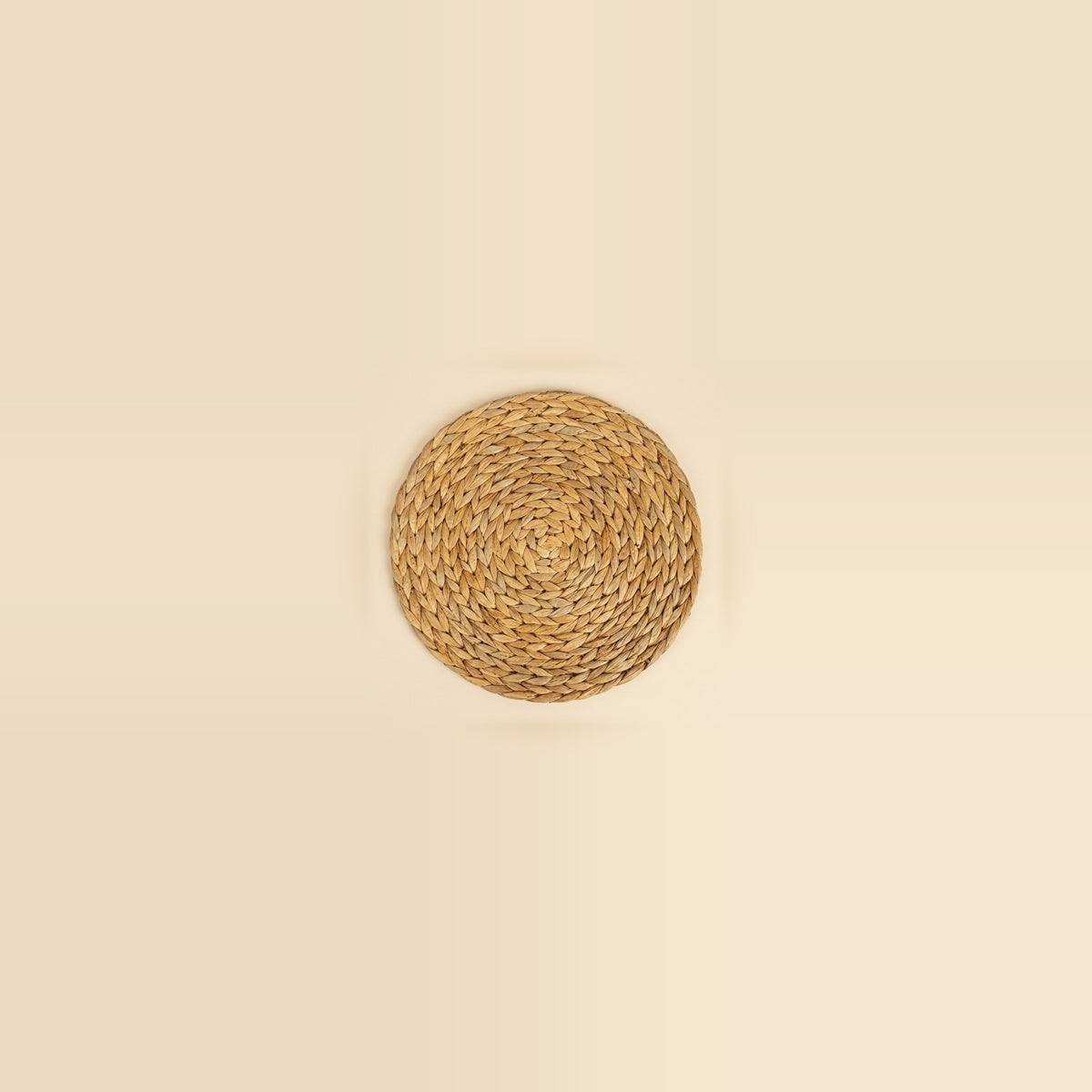 A round woven natural fiber placemat in a light tan color, centered on a solid cream background.