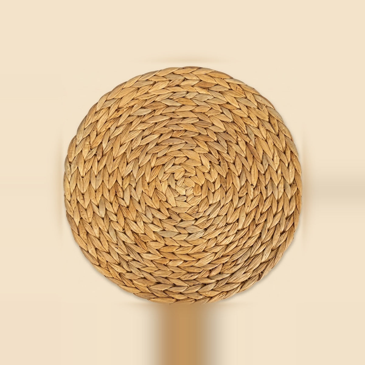 Round tan woven plant-fiber mat with a spiral braided pattern, centered on a pale beige background.