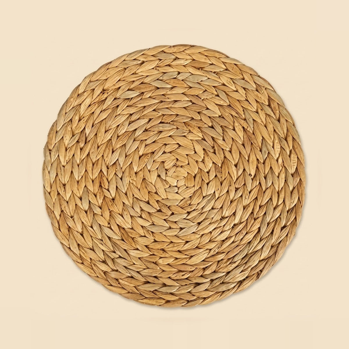 Round golden-tan woven plant-fiber mat with concentric braided rows, shown from above against a pale beige background.