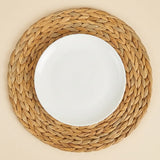 A white plate sits centrally on a round tan braided placemat, viewed from above against a cream background.