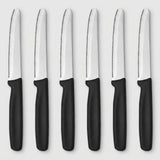Six serrated knives with silver blades and black handles arranged vertically side by side on a light grey background.