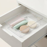 A clear plastic drawer organizer tray holding three pastel cosmetic containers inside an open white drawer.