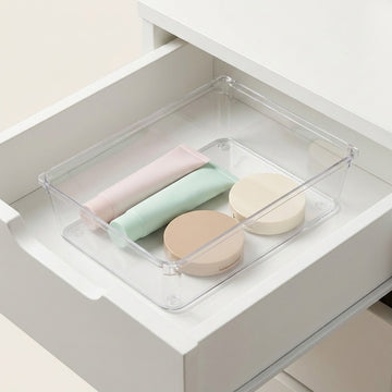 A clear plastic drawer organizer tray holding three pastel cosmetic containers inside an open white drawer.