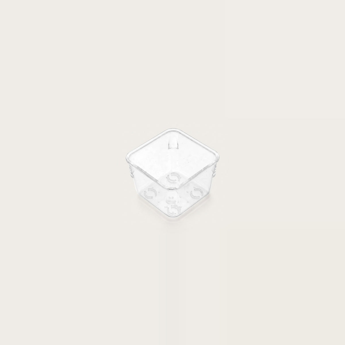 Small clear square organizer tray with rounded corners and circular base details sits centered on an off-white background.