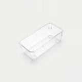 Clear narrow rectangular organizer tray with a dotted base and rounded corners sits diagonally on an off-white background.