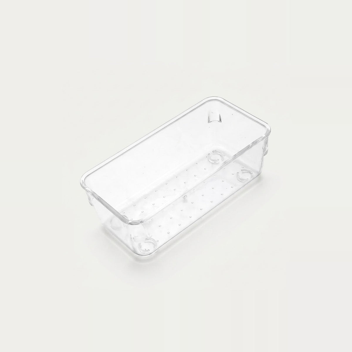 Clear narrow rectangular organizer tray with a dotted base and rounded corners sits diagonally on an off-white background.