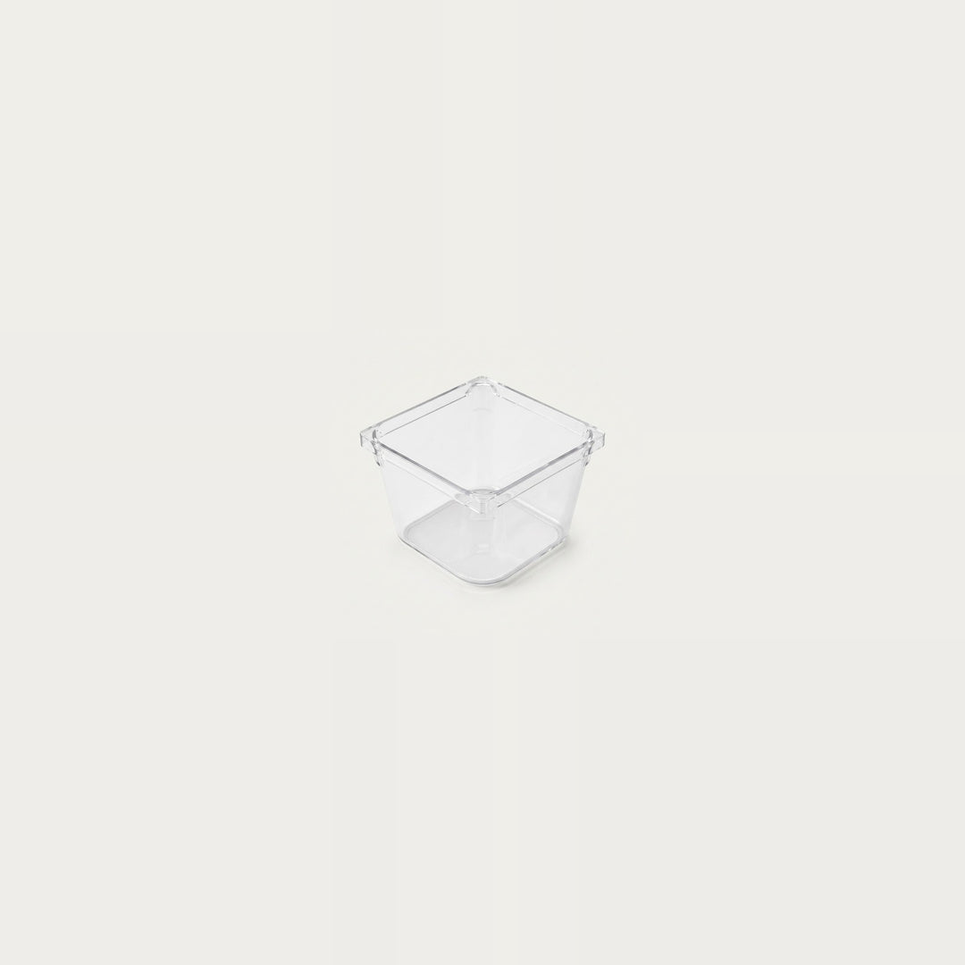 A small empty clear square organizer with smooth sides sits centered against an off-white background.