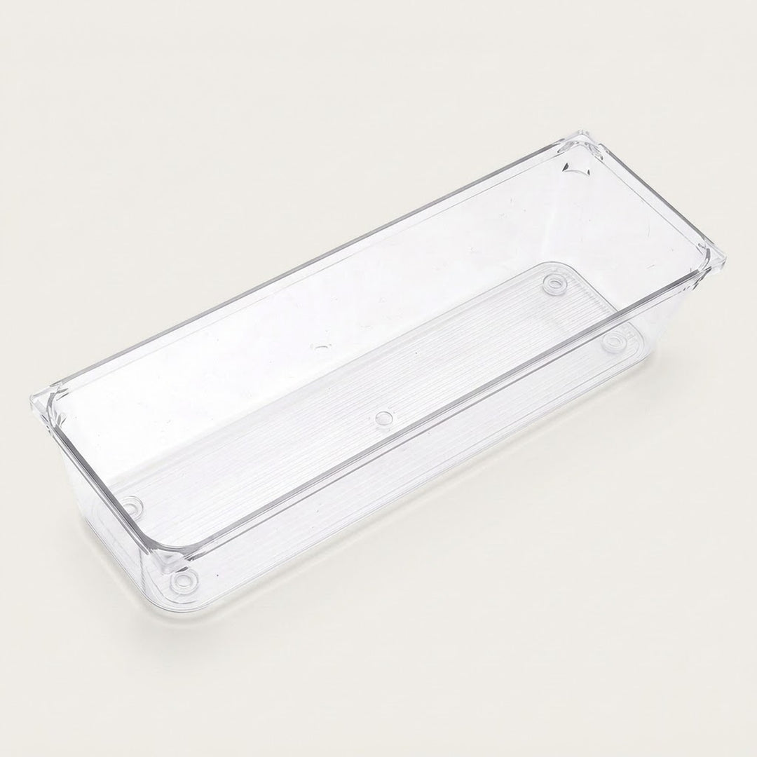 An empty long clear rectangular organizer with smooth sides and rounded corners sits diagonally against an off-white background.