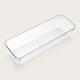 An empty long clear rectangular organizer with smooth sides and rounded corners sits diagonally against an off-white background.