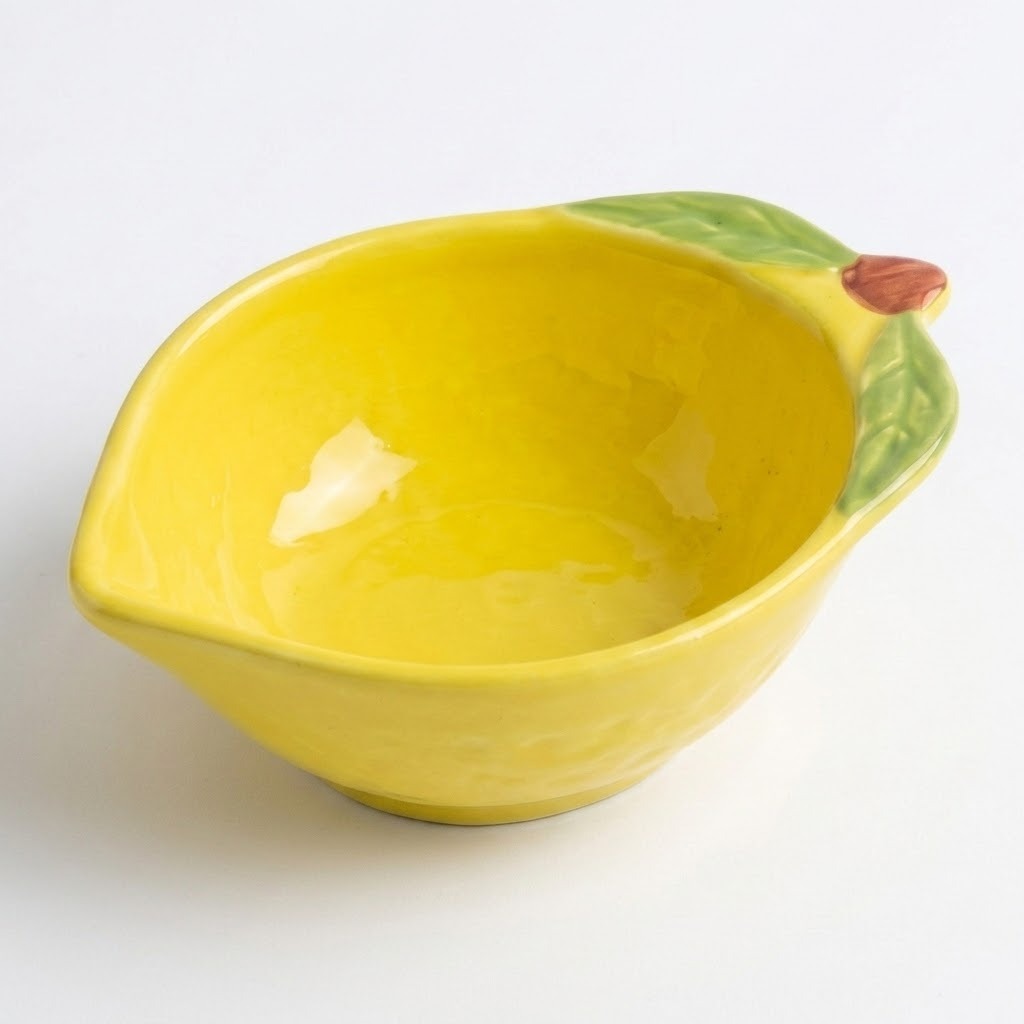 A yellow ceramic bowl designed to look like a lemon, featuring green leaf details on one side and a small brown stem, shown on a plain white background.