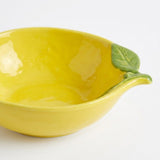 A bright yellow ceramic bowl designed to look like a lemon, featuring a green leaf and stem protruding from the side, set against a plain white background.