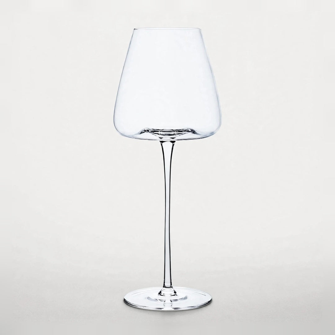 An empty clear wine glass with a tapered bowl, slender stem, and round base stands against a pale background.